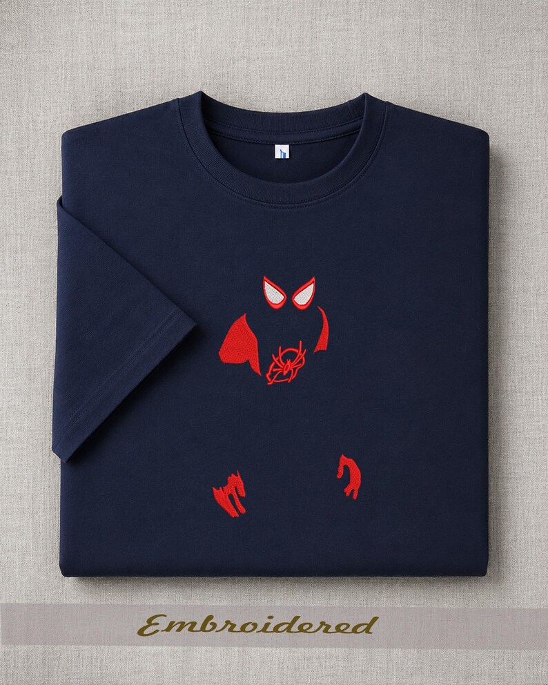 May include: Navy blue t-shirt with a red embroidered Spider-Man design. The design includes the character's eyes, spider emblem, and hands. The word "Embroidered" is printed at the bottom of the image.