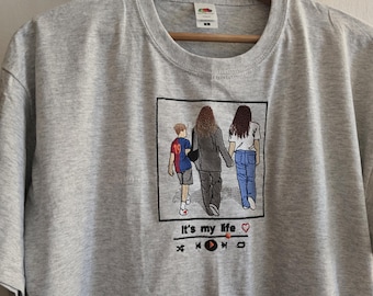 May include: A heather grey t-shirt featuring an embroidered square graphic of three people walking away, with the text "It's my life" and a music player interface icon below the image. The embroidery includes a child in a blue and red jersey.