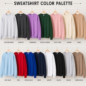 May include: A collection of crewneck sweatshirts displayed on hangers in a colour palette chart. The colours include ash melange, grafite, lavander, bootle green, light pink, cream, sand, sky blue, red, royal blue, navy, white, black, silver, and dark beige.