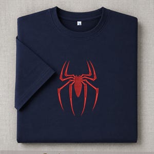 May include: Navy blue t-shirt with a red spider emblem embroidered on the front. The shirt has short sleeves and a crew neck. The word "Embroidered" is printed at the bottom of the image.