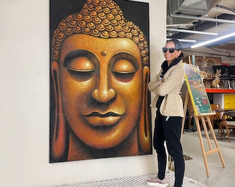 May include: Large, vertical painting of Buddha's face with closed eyes. The artwork features a detailed depiction of the Buddha's face in shades of gold, brown, and orange against a black background. The painting is displayed on a white wall.