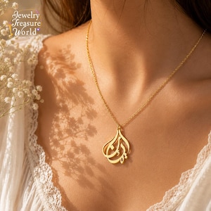 Peut inclure: Un collier doré composé d'une chaîne fine et d'un pendentif orné d'une calligraphie arabe complexe. Le pendentif présente une forme en goutte d'eau et est suspendu à une fine chaîne en métal doré poli qui repose contre le cou.
