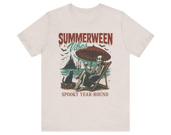 May include: Beige t-shirt with a graphic of a skeleton relaxing on a beach chair under a red umbrella, holding a glass of wine. A black cat sits on a suitcase. The text reads "Summerween Vibes" and "Spooky Year-Round."