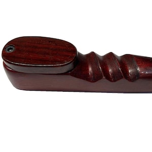 Puede incluir: Una pipa de madera hecha a mano con un rico acabado marrón rojizo oscuro. La pipa presenta un cuenco redondeado, un agarre acanalado y un tallo liso y alargado. El diseño es simple y elegante, mostrando la veta natural de la madera.