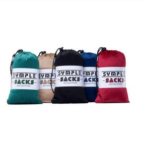 Könnte beinhalten: Fünf Beutel mit Kordelzug in verschiedenen Farben: Türkis, Beige, Schwarz, Marineblau und Rot. Jeder Beutel hat ein weißes Etikett mit dem Text "SYMPLE - SACKS - LARGE PADDED PIPE POUCH" in Schwarz und Grün.