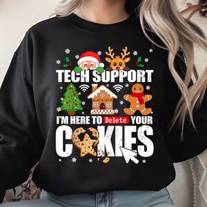 Puede incluir: Sudadera negra con un diseño festivo. El diseño incluye a Papá Noel, un reno, un árbol de Navidad, una casa de jengibre y un hombre de jengibre. El texto dice "TECH SUPPORT" y "I'M HERE TO DELETE YOUR COOKIES."