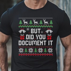 Könnte beinhalten: Schwarzes T-Shirt mit weihnachtlichem Design. Das Design umfasst Rentiere, Weihnachtsbäume, Schneeflocken, Glocken und den Text "BUT DID YOU DOCUMENT IT" in Weiß. Das Shirt hat einen Rundhalsausschnitt und kurze Ärmel.