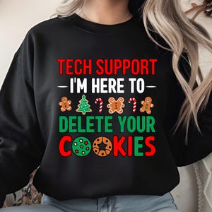 Könnte beinhalten: Schwarzes Sweatshirt mit dem Text "TECH SUPPORT - I'M HERE TO - DELETE YOUR COOKIES" in Rot und Grün. Das Design umfasst Lebkuchenmänner, einen Weihnachtsbaum und Zuckerstangen.