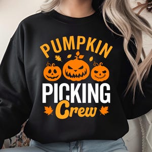 May include: Black sweatshirt featuring the text "PUMPKIN PICKING Crew" in orange and white. The design includes three orange jack-o'-lanterns and orange leaves. A festive autumn-themed garment.