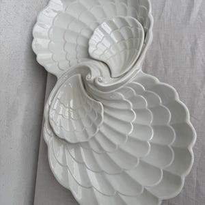 May include: A white ceramic serving dish set in a seashell design. The set includes three shell-shaped dishes of varying sizes, with a glossy finish. The largest dish is approximately 30 cm wide, and the smallest is about 10 cm.