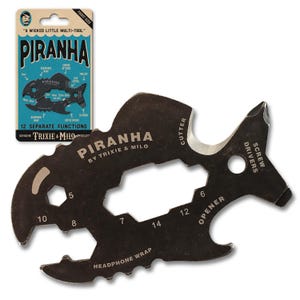 May include: A black multi-tool shaped like a piranha, with the text "PIRANHA" and "TRIXIE & MILO." It has 12 separate functions, including a cutter, screwdriver, and headphone wrap. The packaging reads "A WICKED LITTLE MULTI-TOOL."