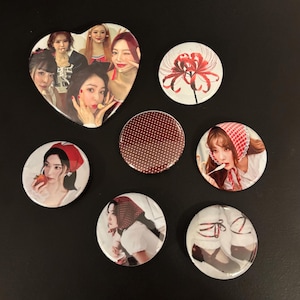 May include: A selection of seven badges, including a heart-shaped one, featuring images of people, a red flower, and a polka dot design. The heart-shaped badge displays a group photo of several people.