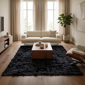 May include: A rectangular black area rug with a thick, textured pile placed on a light wood floor in a living room. The rug is positioned beneath a wooden coffee table, providing a dark contrast to the neutral furniture and decor.