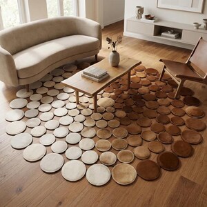 May include: A large circular area rug composed of numerous small, individual circular patches in a gradient of colours ranging from cream and beige to medium brown and dark chocolate, arranged in a radial pattern on a wooden floor.