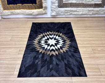 Könnte beinhalten: Ein rechteckiger schwarzer Teppich mit einem geometrischen Sternmuster in der Mitte. Der Stern hat weiße, beige und schwarze Diamanten. Der Teppich besteht aus einem dunklen Material und liegt auf einem Holzboden.