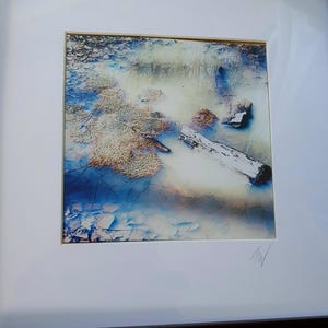Könnte beinhalten: Abstrakter Kunstdruck mit einer ruhigen Wasserlandschaft mit einem weißen Baumstamm, Felsen und strukturierten Bereichen in Blau-, Beige- und Weißtönen. Das Kunstwerk ist in einem weißen Passepartout und Rahmen gerahmt, mit einer Signatur unten rechts.