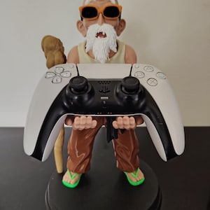 Puede incluir: Una figura de un personaje anciano con barba blanca, gafas de sol naranjas y camiseta sin mangas beige, vistiendo pantalones marrones y chanclas verdes. La figura sostiene un mando de juego blanco y negro y lleva un bastón de madera marrón.