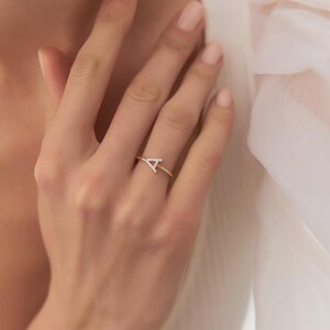 May include: A thin gold ring featuring a capital letter A as the centerpiece. The letter A is embellished with small, clear, sparkling stones set along its surface. The band of the ring is smooth, polished gold, creating a delicate and refined appearance.