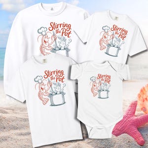 May include: White t-shirts and a sweatshirt featuring a cartoon shrimp chef stirring a pot. The text "Stirring the Pot" is above the shrimp. The image includes a t-shirt, a sweatshirt, and a baby onesie.