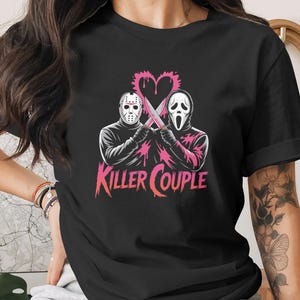 May include: Black t-shirt featuring a graphic of two horror movie characters holding knives, with a pink heart and the words "Killer Couple". The design includes a hockey mask and a Scream mask.