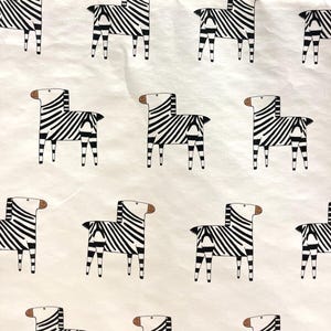 May include: A repeating pattern of stylized zebras in black and white on a cream-colored background. Each zebra is depicted with bold black stripes and a brown head, creating a playful and whimsical design.