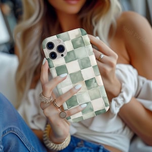 May include: A phone case with a green and white checkered pattern. The case has a watercolor effect and is held by a person. The phone case has a camera module with three lenses.