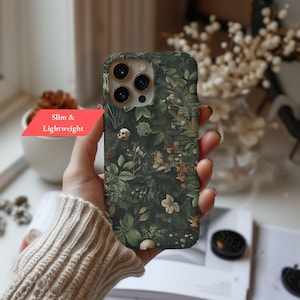 May include: A dark green phone case with a botanical design featuring leaves, flowers, butterflies, and small skulls. The case has a slim and lightweight design, as indicated by the text on a red label.