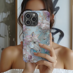 May include: A phone case featuring a detailed illustration of a white unicorn with a flowing mane and horn, surrounded by pastel-colored flowers. The case has a light blue background with a pearlescent effect, and a camera cutout.