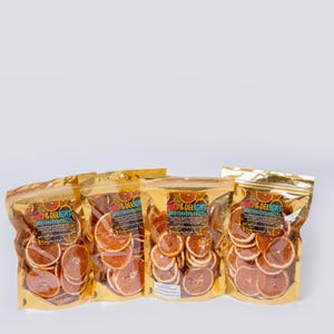 May include: Four gold foil bags filled with dehydrated orange slices. Each bag has a label with the text "DRY & DELIGHT DEHYDRATED FRUITS". The orange slices are a reddish-brown colour and are visible through the clear plastic.