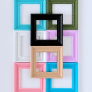 May include: Nine colorful square picture frames in various shades, including black, white, pink, blue, green, and tan. The frames have a beaded border design and are arranged in a grid pattern against a white background.