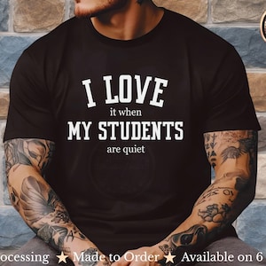 Op de afbeelding: Zwart T-shirt met de witte tekst "I LOVE it when MY STUDENTS are quiet." Het shirt heeft een ronde hals. De afbeelding bevat ook een logo voor "Visimatic Studio Graphic Prints & Gifts."