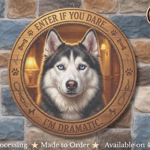 Op de afbeelding: Een rond houten bord met een portret van een zwart-witte Siberische Husky met blauwe ogen. De rand bevat de tekst ENTER IF YOU DARE en I'M DRAMATIC, samen met gegraveerde iconen van pootafdrukken, botten, hondenriemen en kleine honden.