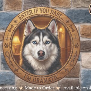 Op de afbeelding: Ronde houten bord met een Husky-hondenportret met blauwe ogen en de tekst "ENTER IF YOU DARE... I'M DRAMATIC." Het bord is versierd met pootafdrukken, botten en touwen. De achtergrond is een veelkleurige stenen muur.