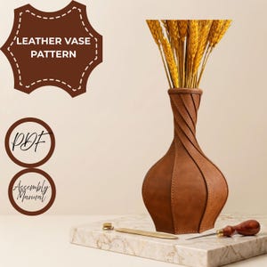 May include: A brown leather vase with a twisted panel design containing yellow wheat stalks. Text reads LEATHER VASE PATTERN, PDF, and Assembly Manual. A metal tool and a wooden awl are placed on the surface next to the vase.
