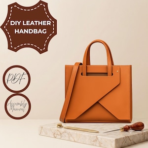 May include: A tan leather handbag with a structured square shape, two top handles, and a diagonal front flap. Text on the image reads DIY LEATHER HANDBAG, PDF, and Assembly Manual. A metal tool and a wooden awl rest on a marble surface.