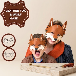 May include: Two brown leather fox masks with white accents and black noses. The image includes text reading LEATHER FOX & WOLF MASK, PDF, and Assembly Manual. A metal tool and a wooden-handled awl rest on a stone surface in the foreground.