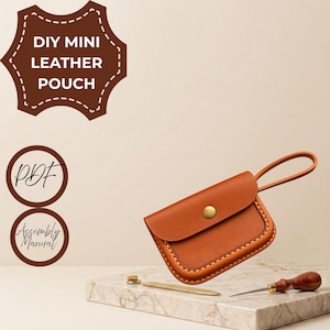 May include: A tan leather pouch with a brass snap closure and a wrist strap, featuring visible stitching along the edges. Text in the image reads DIY MINI LEATHER POUCH, PDF, and Assembly Manual. A metal tool and an awl are placed nearby.
