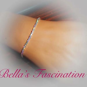 May include: A delicate, sparkling bracelet with numerous small, iridescent stones. The bracelet is set against a neutral background, with the text "Bella's Fascination" in a cursive font at the bottom.