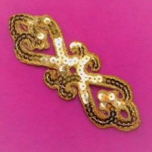 May include: Ornate gold sequin applique with a symmetrical design. The applique features gold sequins, black thread outlining, and white accents. The decorative embellishment is set against a vibrant pink background.