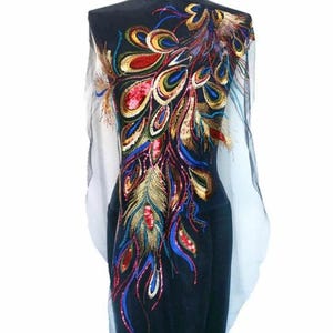 Könnte beinhalten: Schwarzer Stoff mit einem farbenfrohen Pfauenfedermuster. Das Design zeigt rote, goldene, blaue und grüne Pailletten und Stickereien. Der Stoff ist über einer Schaufensterpuppe drapiert.