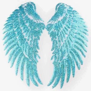 May include: Two matching, light blue sequined angel wings on a white background. The wings are symmetrical, with a feathery design and a gradient effect, transitioning from a darker blue at the edges to a lighter blue in the center.