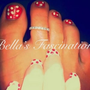 Puede incluir: Primer plano de un pie con uñas rojas con lunares blancos. Un anillo plateado adorna un dedo del pie. El texto "Bella's Fascination" está en la imagen. Las uñas están pintadas con base blanca y lunares rojos.