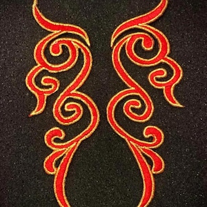 May include: Two embroidered appliques with a symmetrical design. Each applique features a vibrant red, swirling pattern outlined in gold thread. The appliques are set against a black background, highlighting the intricate details of the design.