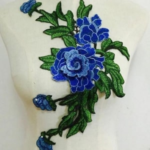 May include: A blue floral embroidered applique featuring detailed blue flowers and green leaves. The applique is designed with a three-dimensional effect, showcasing intricate stitching and a vibrant color palette. This decorative element is suitable for various craft projects.