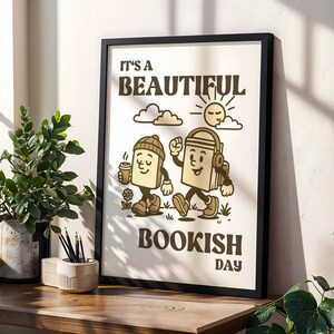 Könnte beinhalten: Ein gerahmter Kunstdruck mit dem Text "IT'S A BEAUTIFUL BOOKISH DAY" und Illustrationen von zwei Buchfiguren. Eine Buchfigur hält eine Kaffeetasse, die andere trägt Kopfhörer. Das Kunstwerk ist in Braun- und Beigetönen gehalten.