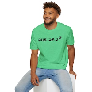 May include: A green t-shirt with the text "GIRL DAD²" in black and green. The shirt is short-sleeved and made of a soft material. The person in the image is wearing blue jeans.