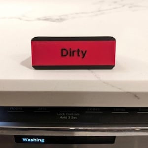 May include: A rectangular dishwasher magnet with a black frame and a bright red center panel. The word Dirty is printed in bold black sans-serif capital letters in the middle of the red section. The magnet has a smooth, matte finish.