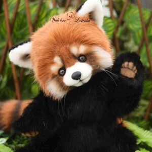 Puede incluir: Un peluche de panda rojo con cabeza marr&oacute;n y blanca, cuerpo negro y una pata saludando. El juguete tiene una expresi&oacute;n amigable y el texto "With love Lazenka" es visible.