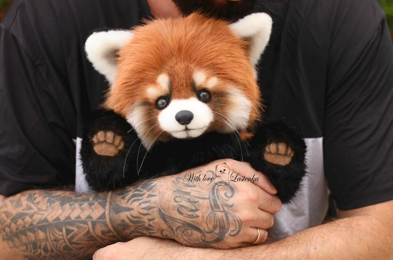 Puede incluir: Un peluche de panda rojo con una cabeza marr&oacute;n rojiza y esponjosa, orejas blancas y patas negras. El juguete tiene una nariz negra y bigotes. El texto "With love Lazienka" es visible en la imagen.