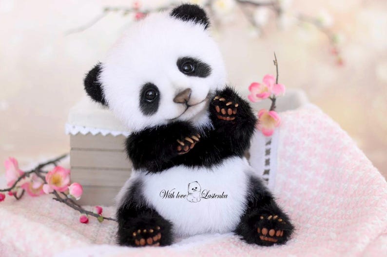 May include: A plush panda bear with black and white fur, black paws, and a friendly expression. The panda is holding its paws up and has the text "With love Lasienka" on its belly. Pink flowers are in the background.